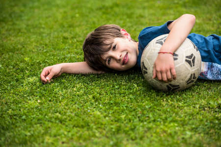 Child with soccer ball lying on the grass and relax with smiling after playing footballの写真素材