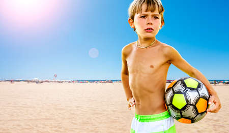 Portrait of a smiling child with a soccer ball in his hand, at the beach by the sea.の写真素材