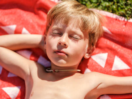 Portrait of a smiling baby in a bathing suit who is resting lying on a towel resting on the grass on a sunny day. On vacation in the summer.の写真素材