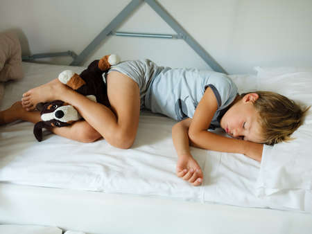 Child in pajamas sleeping in his bed without blankets, illuminated by the light that filters through...