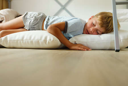 Child in pajamas sleeping in his bed without blankets, illuminated by the light that filters through...