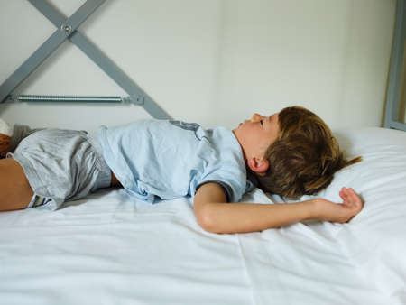 Child in pajamas sleeping in his bed without blankets, illuminated by the light that filters through...