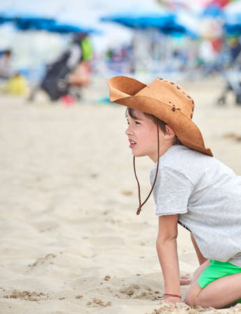 Happy child with cowboy leather hat playing with sand. Close-up of a smiling child with cowboy hat, at the beach by the sea.の写真素材