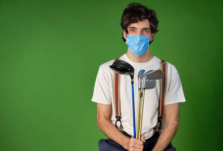 Golfer in casual clothing and with a protective covid-19 mask, he is holding some golf irons and a golf drive.の写真素材