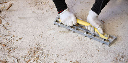 Craftsman in workwear who, using the rabot, removes excess glue left on the floor after removing the wooden parquet glued to the slab of an apartment. Worker at work while performing home renovation.の写真素材
