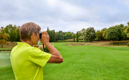 The golfer accurately measures the distance to the flag in a golf course with the laser rangefinder. In the background the forest.の写真素材