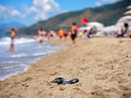 Flip flops on the Italian beach on a sunny summer morning, in the background bathers cooling off in the Tyrrhenian Sea in the Gulf of Policastro, Italy.の写真素材