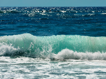Rough sea with emerald green waves crashing on the beach. In the background the blue sea with sun...