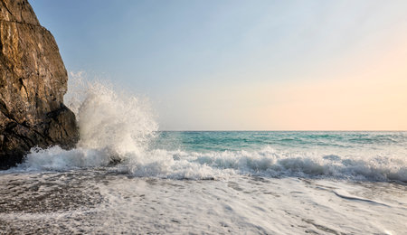 Rough sea with emerald green waves crashing on the rocks and on the beach. In the background the...