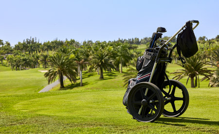 Golf cart with bag and golf clubs in the fairway of a golf course, parked at the edge of the green.の写真素材