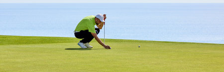 Golfer on the green with a putter in his hands. A player on the green evaluates the slopes and distance from the hole before aiming the ball towards the flag.の写真素材