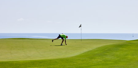 Golfer on the putting green with golf iron, early in the morning during a golf competition. The golfer hits the ball into the hole.の写真素材