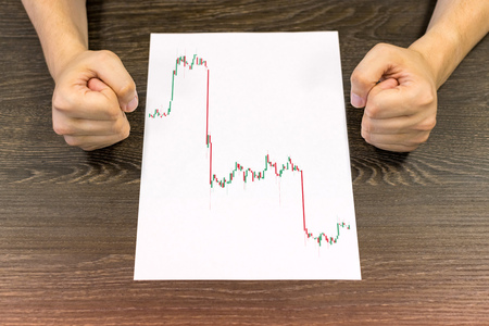 Businessman sitting at table. There are sheet of paper with a trading chart on the table. Angry...