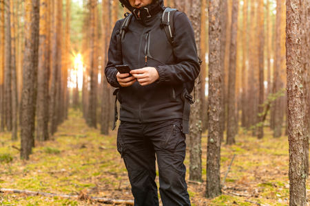 Tourist traveler man lost in pine forest and looks at smartphone screen. Looks for the right way.