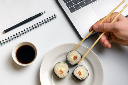 Break time for sushi eating. Sushi rolls snacking at work. Laptop and notebook on white organized desk.の写真素材