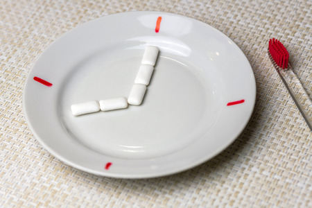 Teeth cleaning break concept. Time to your teeth brushing during work or eating. Clock symbol on plate. Teeth protect from tooth decay or plaque concept.の写真素材