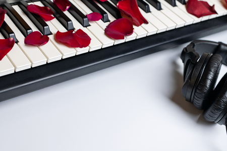 Piano keys strewn with red rose petals and headphones, isolated, copy space. Romantic concept. Classical music instrument for playing romantic music.の写真素材