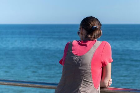 Woman dreams of traveling and looks at sea. Rear back view, copy space. Waiting for a lover or...