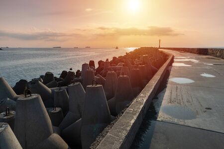 North pier with breakwaters, sunset seascape. Tetrapods along edges of pier. Beautiful evening seascape. Modern lighthouse in sunlight.の写真素材