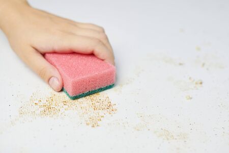 Cleaning kitchen table. Pink sponge in woman hand removes dirt, bread crumbs and leftovers....