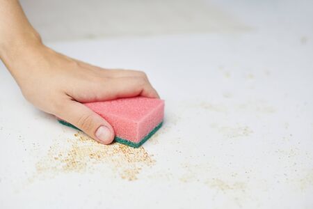 Cleaning kitchen table. Pink sponge in woman hand removes dirt, bread crumbs and leftovers. Household choresの写真素材