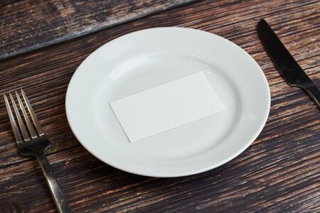 Empty plate on table with cutlery and blank business card, top view. Message for visitor of restaurant or cafe. Business lunch without tips concept.の写真素材