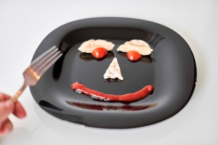 Food face, funny dumpling and ketchup. Smiling face on plate. Food art on black plate. Motivation for losing weight and healthy eating.の写真素材