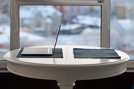 Home workplace in modern loft apartment. Laptop on white table, cityscape in window background. Cozy...