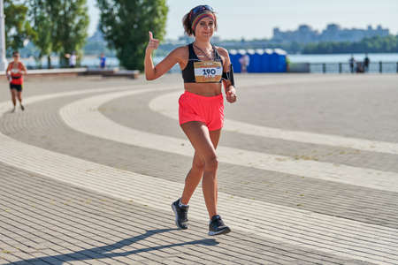 Voronezh, Russia - 08.24.2019 - Young girl runs along road. Runners marathon and championship competition, copy space. Street sprinting outdoors. Healthy sport event.のeditorial素材