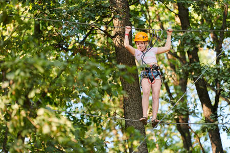 Girl in high ropes experience adventure tree park. Rope road course in trees. Climbing adventure rope park. Wood bridge and high wire activity.のeditorial素材