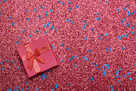 Red gift box on festive glitter. Little closed box with bow and gift for anniversary or wedding....