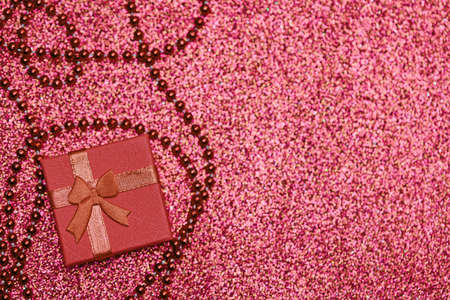Red gift box on festive glitter, copy space. Little closed box with bow and gift for anniversary or wedding. Surprise giftbox for loved one.の写真素材