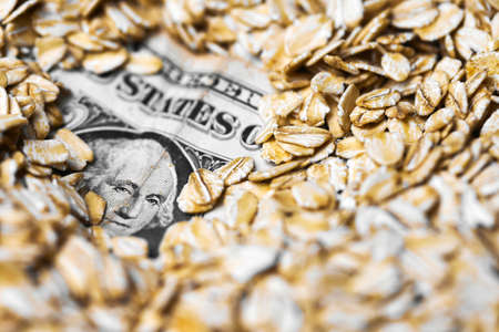 Dollar money in oat flakes. Oat export prices, economic concept. Decrease or increase in price of rolled oats production. American dollar in scattering of oatmeal groats.の写真素材