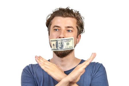 Money on man mouth. Bribe, corruption concept. Man in blue t-shirt with dollars on white isolated backgroundの写真素材