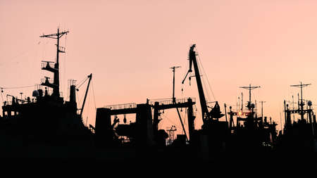 Silhouettes of ships and container cranes in sea port, sunset background. Scenery industrial landscape.の写真素材