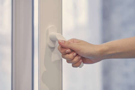 Woman holding white modern handle at PVC plastic window with double glazing, opening and closing frame. Close up.の写真素材