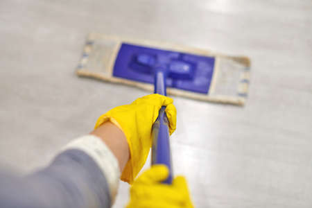 Young woman in protective yellow rubber gloves using flat wet mop while cleaning floor in house.の写真素材