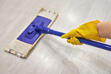 Young woman in protective yellow rubber gloves using flat wet mop while cleaning floor in house.