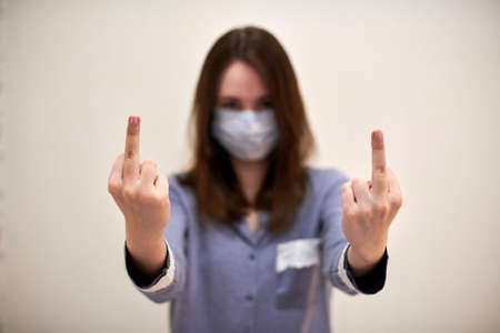 Young brunette woman in medical protective mask showing fuck you gesture. Portrait, blurred face....