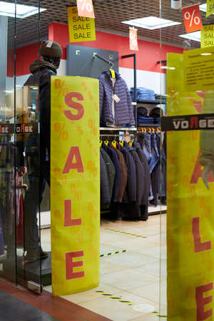 Russia, Kaliningrad - 02.26.2021 - Seasonal sale in outwear shop at european shopping center. Yellow billboards with sale text, holiday discounts in shopping mall. Promotions in clothing store.のeditorial素材