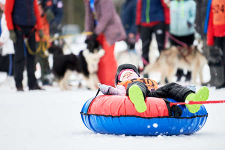 VERKHOSHIZHEMYE, RUSSIA - 03.07.2020 - Little kid on snow tubing with sled dog. Funny winter sport activity, ride on inner tube. Happy family leisure in holidays. Snowtubingのeditorial素材