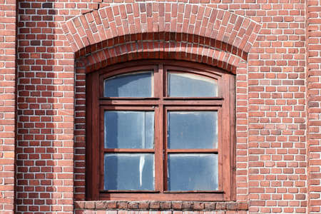 One arched glass window on old red brick wall. Vintage window in brown wooden frame on red brick...
