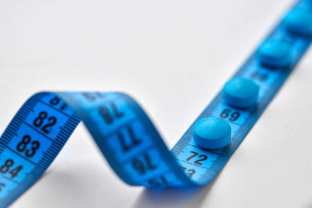Blue round diet pills and measuring centimeter tape isolated on white background. Diet, slimming, weight loss concept.の写真素材