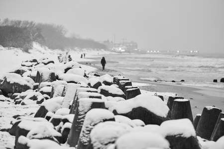 Concrete breakwaters covered with snow against background of winter sea. Coastal protection in snow. Snowy cloudy seascape.の写真素材