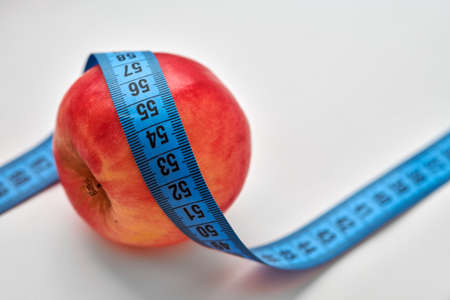 Red apple with blue measuring tape around it isolated on white background. Diet, proper nutrition...