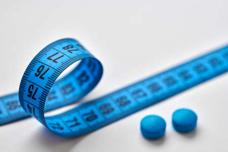 Blue round diet pills and measuring centimeter tape isolated on white background. Diet, slimming, weight loss concept.の写真素材