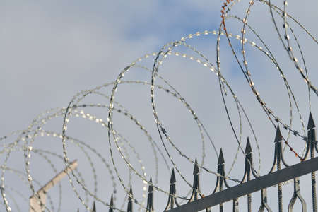 Barbed wire on fence, steel grating fence, metal fence wire. Coiled razor wire with sharp steel...