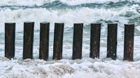 High wooden breakwaters in blue foaming sea waves, close up view. Long poles or groynes in water....