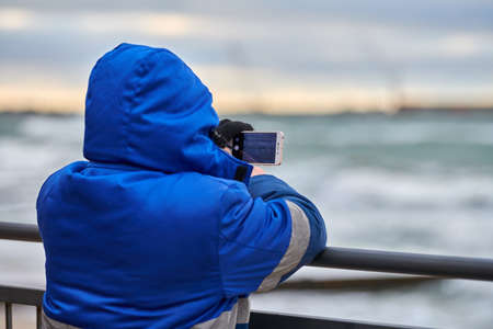 Back view of man tourist taking photo of seascape with smartphone. Taking pictures of sea landscape...