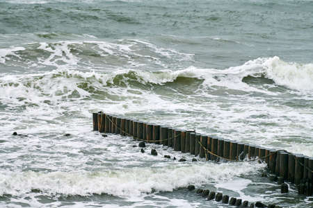 Scenic view of blue sea with bubbling and foaming waves. Vintage long wooden breakwaters stretching...